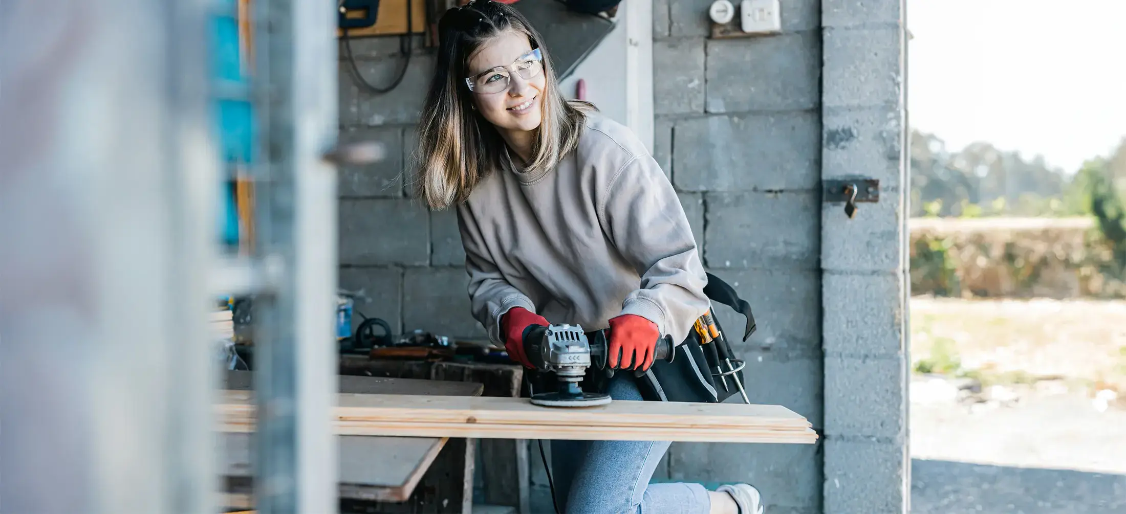 A young person is using an electric sander on wood, in a workshop